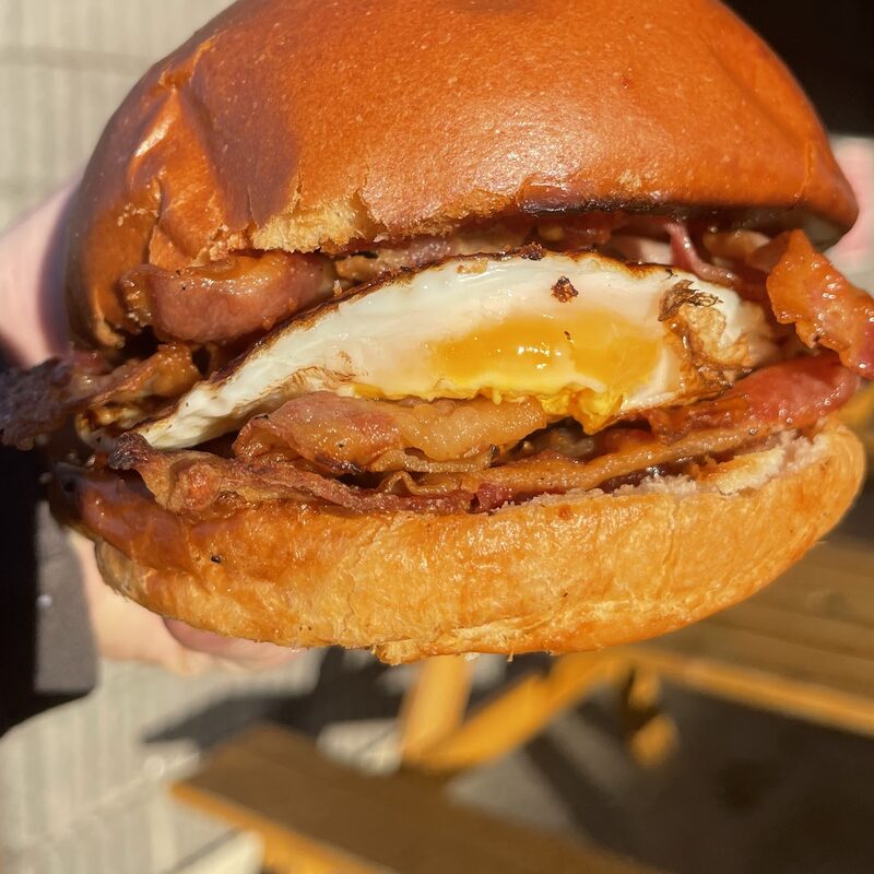 A toasted brioche bap with bacon and a fried egg.