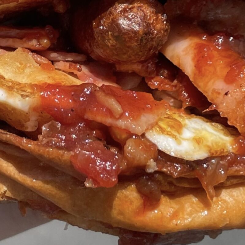 Close view of a bap filled with sausage, bacon, egg and beans.